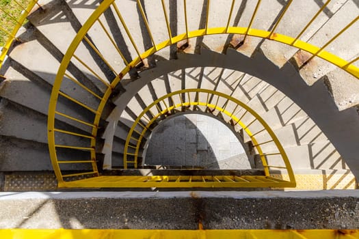 Top view of a concrete spiral staircase with yellow railings on a sunny morning