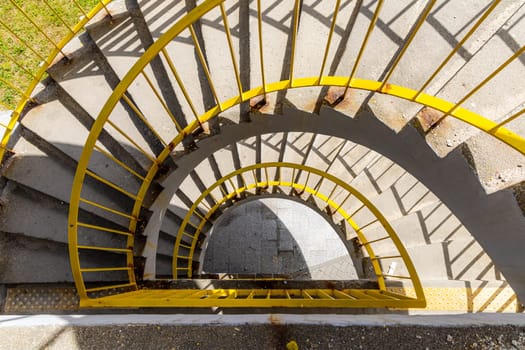 Top view of a concrete spiral staircase with yellow railings on a sunny morning