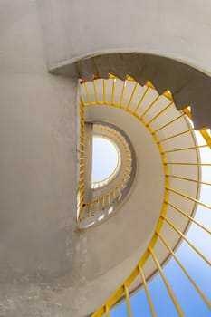 Bottom view of a concrete spiral staircase with yellow railings on a sunny morning