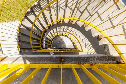 Top view of a concrete spiral staircase with yellow railings on a sunny morning