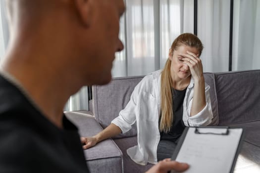 A male psychologist consults a female patient, makes notes. A woman emotionally talks about herself, covering her face with her hands.