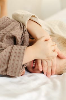 The brothers lie in dressing gowns in a white bed, play, hug, smile. Family concept. Close-up.