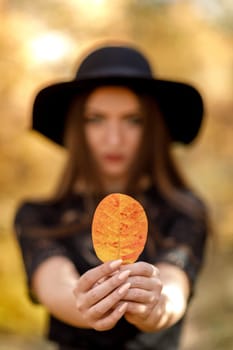 portrait of beautiful woman in black hat with yellow autumn leaf. focus on leaf