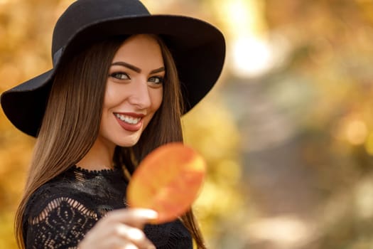 Close-up portrait of beautiful woman in black hat with yellow autumn leaf