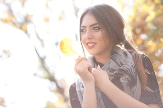 Close-up portrait of beautiful woman in gray scarf with yellow autumn leaf. high key