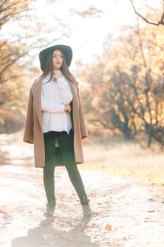 beautiful young woman in coat and black hat in park in the autumn. high key