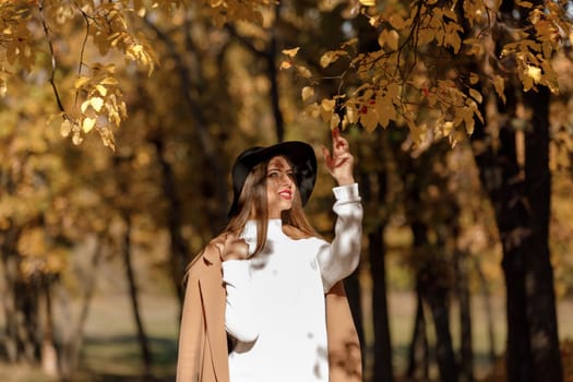 beautiful young woman in coat and black hat near tree in the autumn