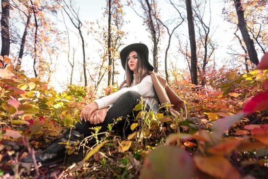 beautiful happy woman in coat and hat in forest on a background of yellow autumn foliage