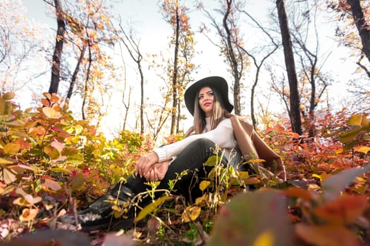 beautiful happy woman in coat and hat in forest on a background of yellow autumn foliage