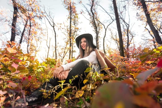 beautiful happy woman in coat and hat in forest on a background of yellow autumn foliage