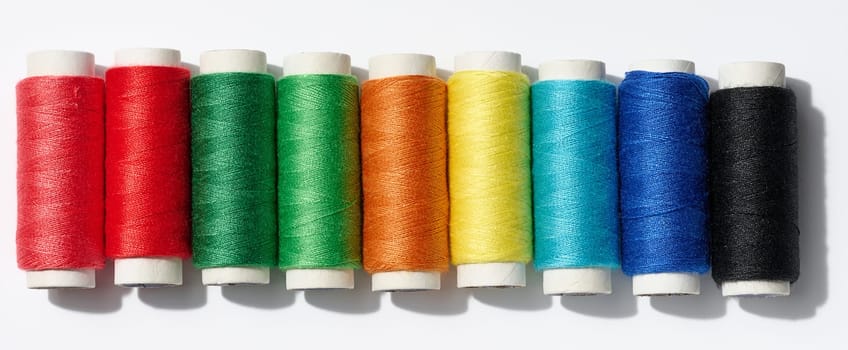 Multicolored spools of sewing threads on a white background, top view
