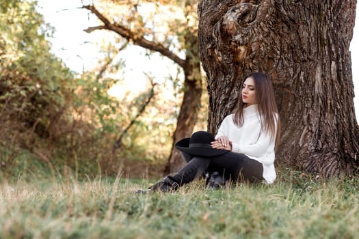 beautiful woman sitting under big tree and daydreaming on sunny autumn day.