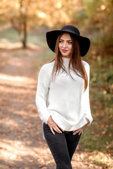 beautiful young woman in black hat posing in park in the autumn