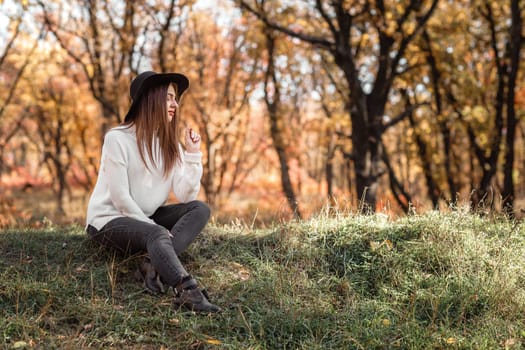 beautiful smiling woman sitting on grass and daydreaming on sunny autumn day. copy space