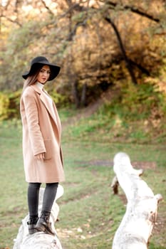 beautiful young woman in coat and black hat posing in park in the autumn