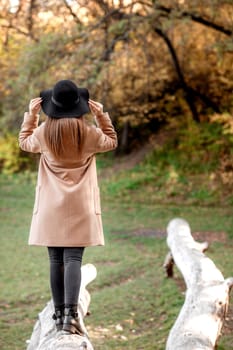 beautiful young woman in coat and black hat posing in park in the autumn. back view