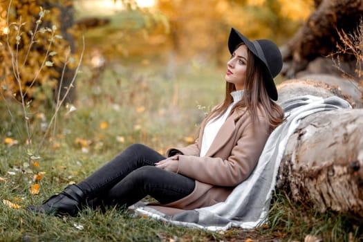 beautiful woman in black hat sitting near tree and dreams on sunny autumn day.