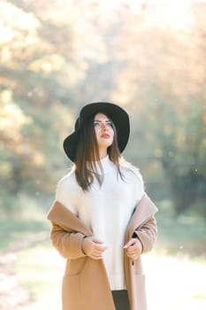 portrait of beautiful young woman in coat and black hat in park in the autumn. high key