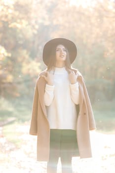 beautiful young woman in coat and black hat in park in the autumn. high key