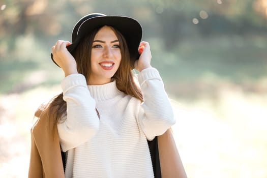 portrait of beautiful happy smiling woman in coat and black hat in park in the autumn. high key