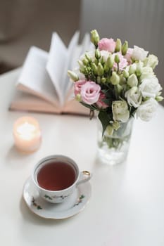 Romantic Spring still life. Romantic background with cup of tea, rose flowers and open book over white table