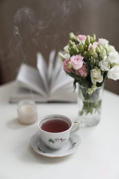 Romantic Spring still life. Romantic background with cup of tea, rose flowers and open book over white table