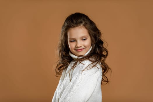 Cute shy little child girl in white sweater on beige background. Human emotions