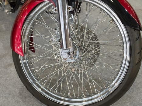 Beautiful nickel plated front wheel of a red motorcycle.