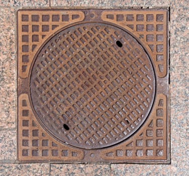 Old rusty sewer hatch on an old metal plate. View from above.