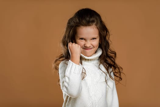 angry screaming little child girl in white sweater mad raising fist frustrated and furious. Human emotions and facial expression