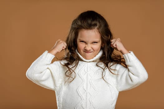 angry screaming little child girl in white sweater mad raising fist frustrated and furious. Human emotions and facial expression