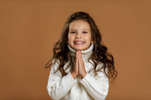happy beautiful curly little girl in white sweater asking for something. Dream come true