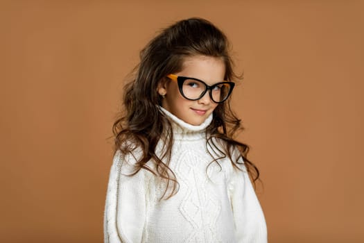 Cute curly little child girl wearing glasses and looking to camera in studio