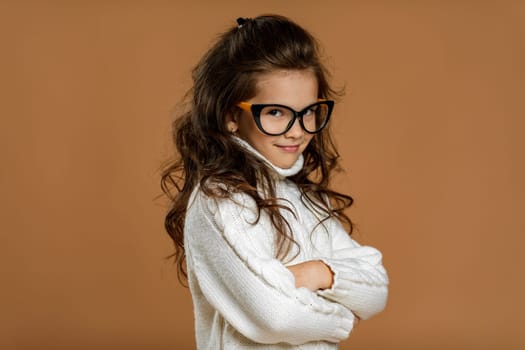 Cute curly little girl wearing glasses and looking to camera in studio. child stares