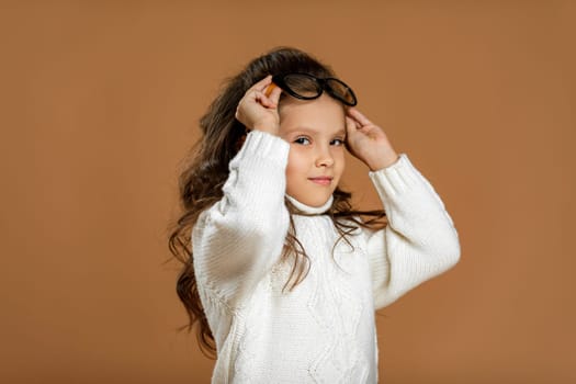 Cute curly little child girl wearing glasses and looking to camera in studio
