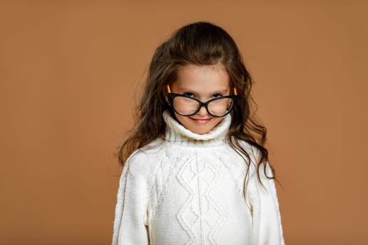 Cute curly little girl wearing glasses and looking to camera in studio. child stares