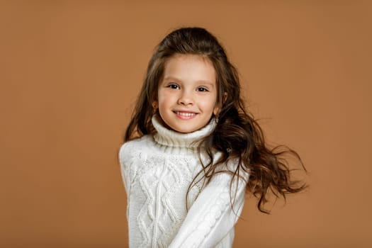 Cute smiling little child girl in white sweater looking to camera on beige background. child with flying hair