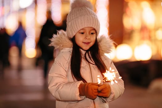 Cute smiling little girl with bengal lights on the street in the evening in winter. Christmas holidays