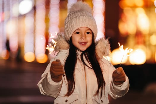 Cute smiling little girl with bengal lights on the street in the evening in winter. Christmas holidays