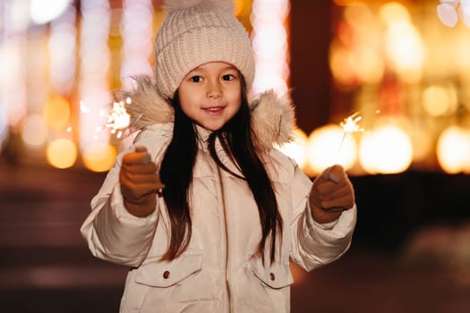 Cute smiling little girl with bengal lights on the street in the evening in winter. Christmas holidays