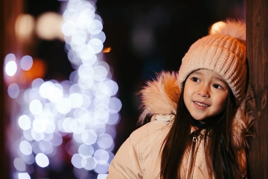 portrait of cute smiling little girl in a knitted hat outdoor in the evening in winter. background with bokeh