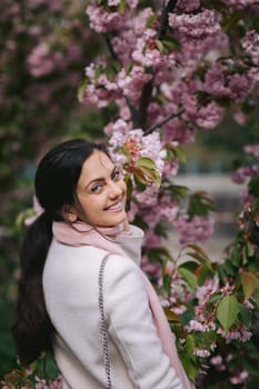 Beautiful young brunette woman enjoying spring day in park during Sakura cherry blossom season