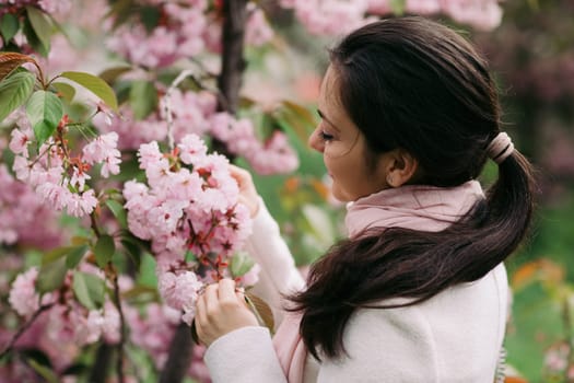 Beautiful young brunette woman enjoying spring day in park during Sakura cherry blossom season