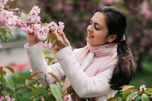 Beautiful young brunette woman enjoying spring day in park during Sakura cherry blossom season