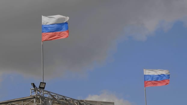 Russian flag on the flagpole waving in the wind against a blue sky with clouds.
