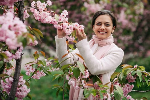 Beautiful young brunette woman enjoying spring day in park during Sakura cherry blossom season