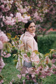 Beautiful young brunette woman enjoying spring day in park during Sakura cherry blossom season