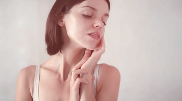 A young girl touches her delicate, clean, moisturized face skin with her hands, a woman takes care of the health and beauty of her body in the bathroom.