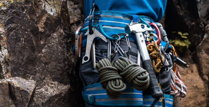 Climbing equipment, ropes, carabiners, harness, belay, hammer close-up of a rock-climber put on by a man, the traveler leads an active lifestyle and is engaged in mountaineering.