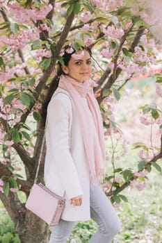 Beautiful young brunette woman enjoying spring day in park during Sakura cherry blossom season